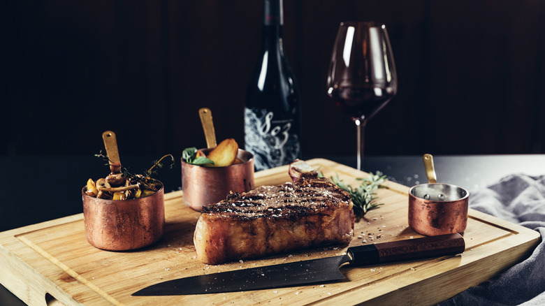 Steak on wood cutting board with copper bowls and wine glass