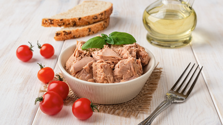 canned tuna in bowl alongside basil, cherry tomatoes, and bread
