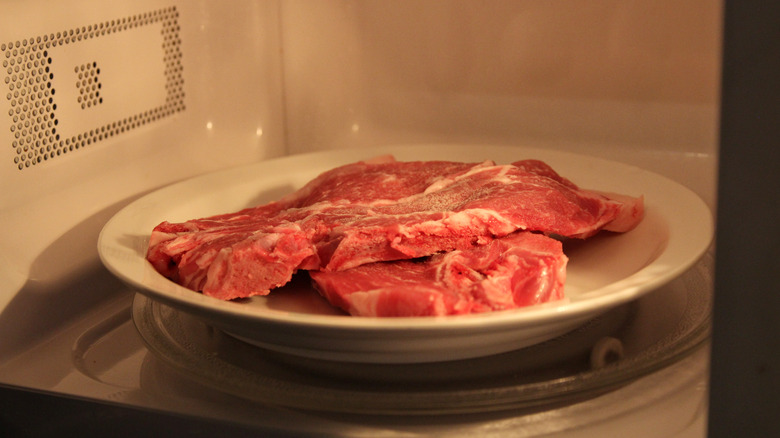 Raw steaks on a plate in the microwave