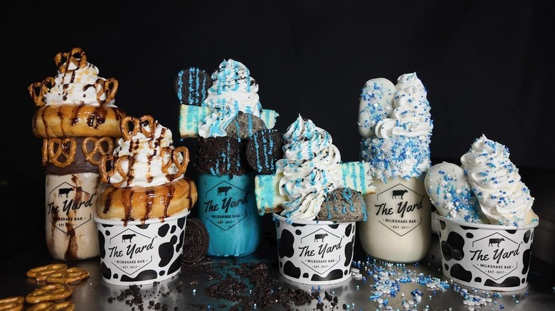 A selection of milkshakes and cups of ice cream from the Yard, each topped with whipped cream, drizzle, sprinkles, cookies, or pretzels and a doughnut