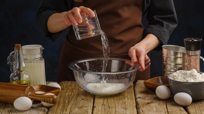 Hands adding water to bowl with yeast