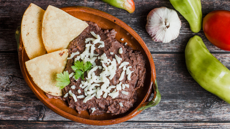 Ceramic bowl of black refried beans with tortilla chips and cheese