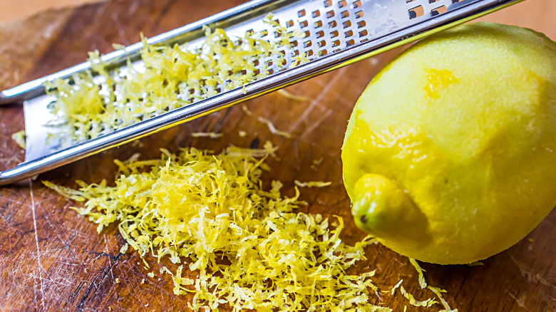 lemon being grated with zest on cutting board