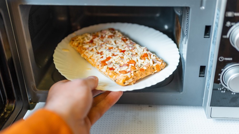 Frozen pizza slice or small pizza going in oven