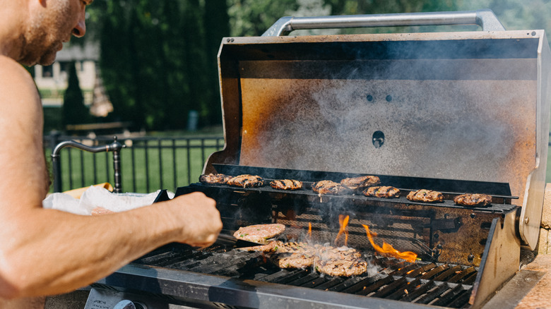 Man cooks burgers on a grill with a dirty inside lid