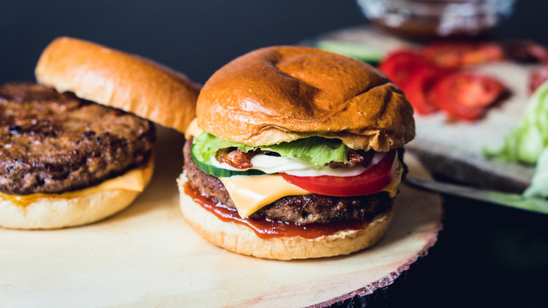 Cheeseburgers on a wooden plate with lettuce and tomato slices blurred in the background