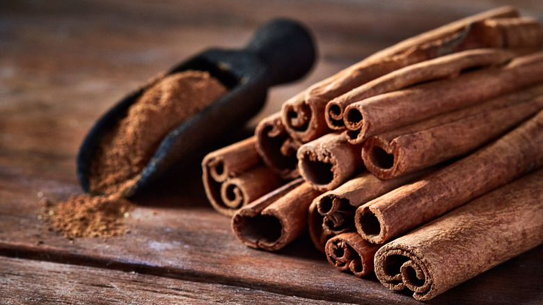 Cinnamon sticks and scooper of ground cinnamon on a wooden table.