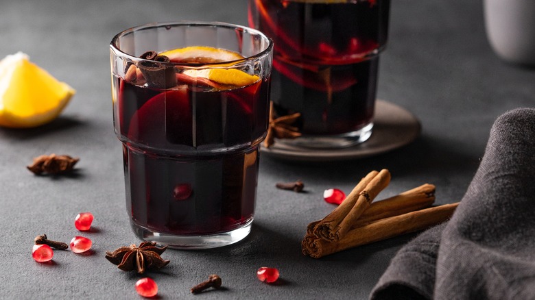 A glass of mulled wine surrounded by spices and pomegranate seeds