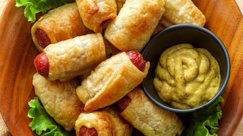 Pigs in a blanket on a serving platter with a ramekin of mustard.