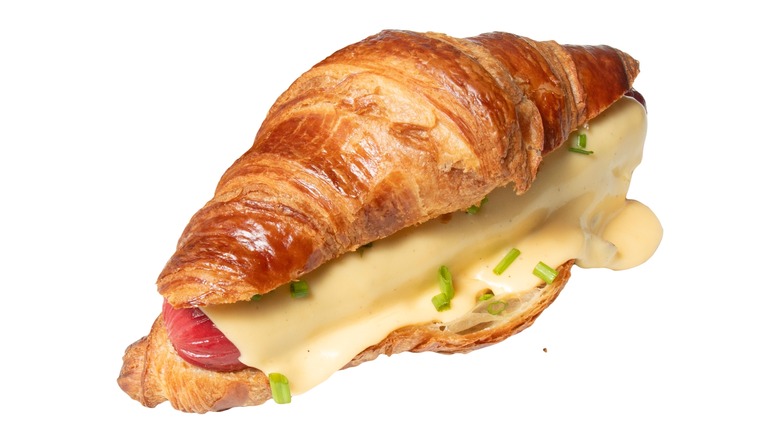 Hot dog in a croissant with cheese sauce and chives