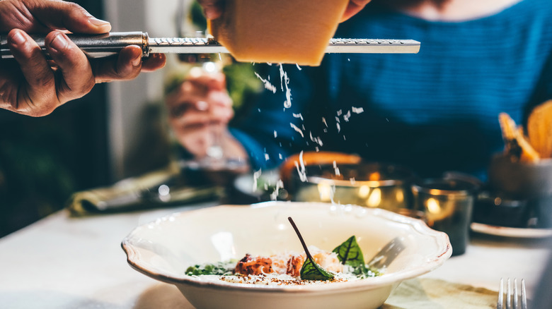 waiter grates cheese over bowl