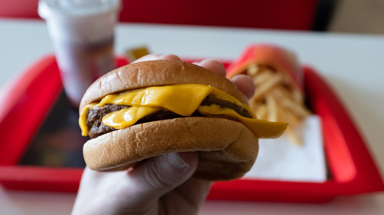 Hand holds a burger inside fast food restaurant