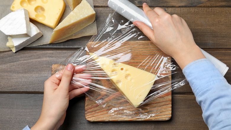 person wrapping cheese in plastic wrap