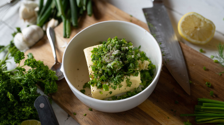 White bowl of butter with fresh herbs, lemon, and garlic