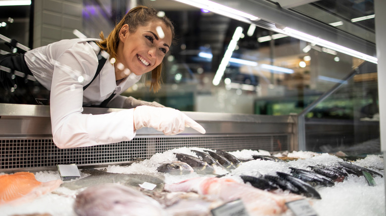 Woman selling fish from fishmonger display in store