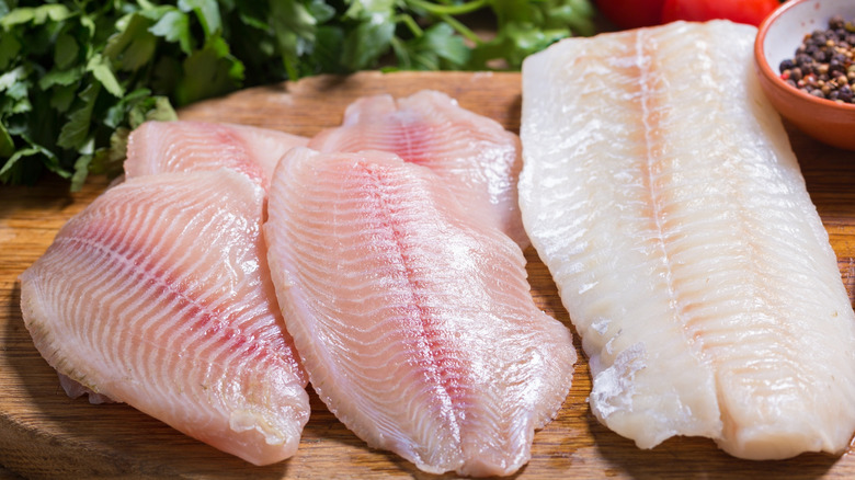 Raw tilapia and cod on wooden board