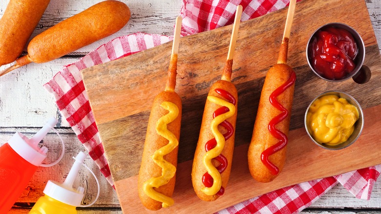 Corn dogs on wood board with ketchup and mustard