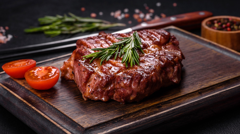 A cooked steak sits on a wooden cutting board, garnished with rosemary