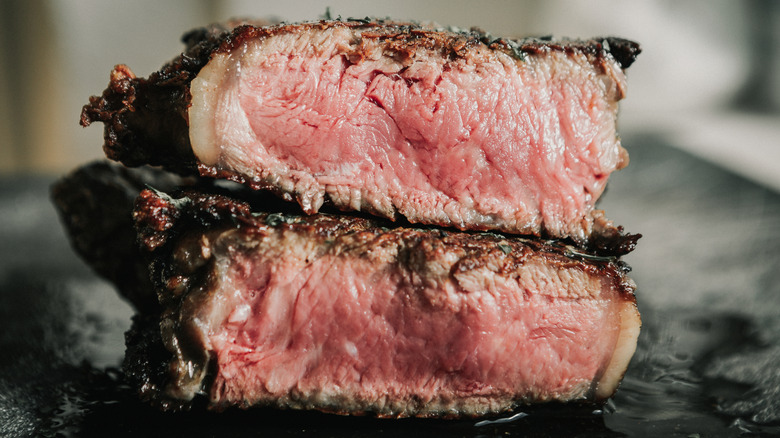 Two parts of steak sit stacked on top of each other, revealing a medium-rare cook