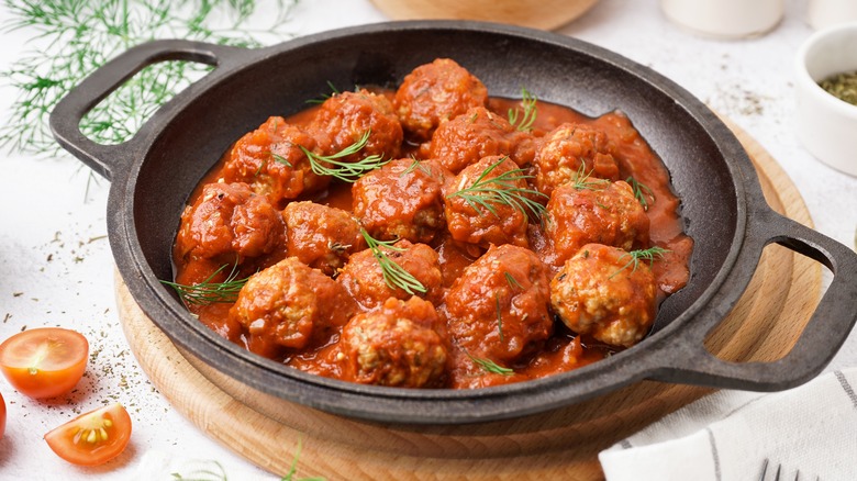 Cooked meatballs in a bed of marinara sauce in a black pan