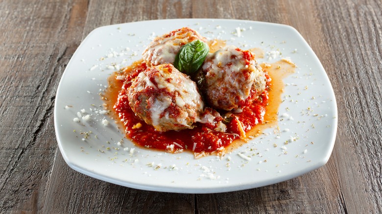 Three meatballs filled with cheese and topped with marinara sauce sit on a white plate