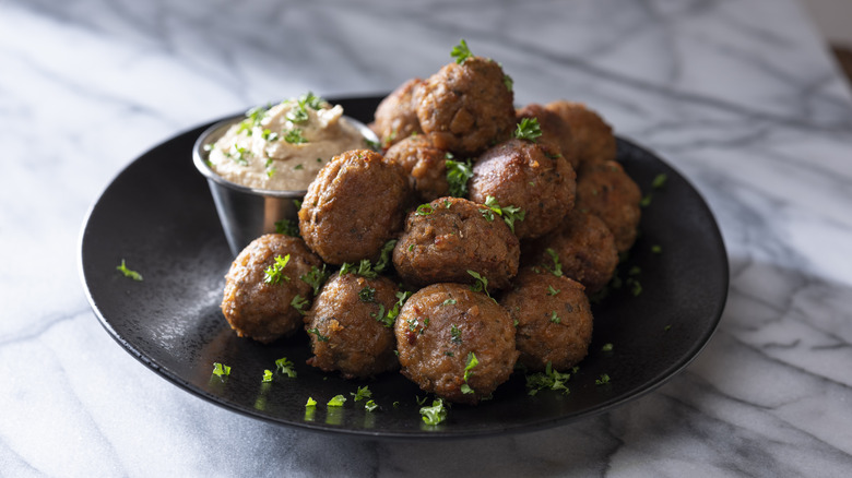 Meatless meatballs garnished with parsley sit on a black plate with a side of hummus