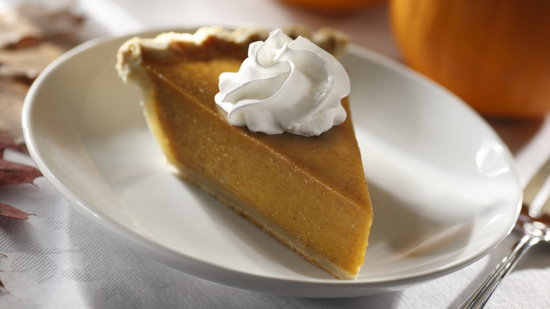 Slice of pumpkin pie with whipped cream in white shallow bowl