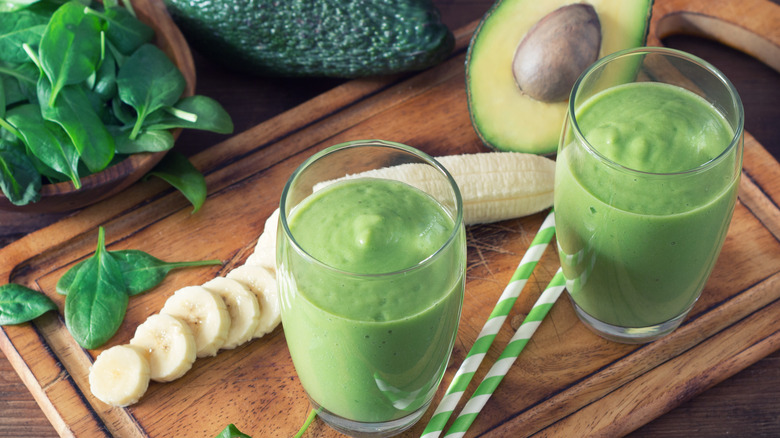 Two glasses of avocado green smoothies with banana and spinach on cutting board