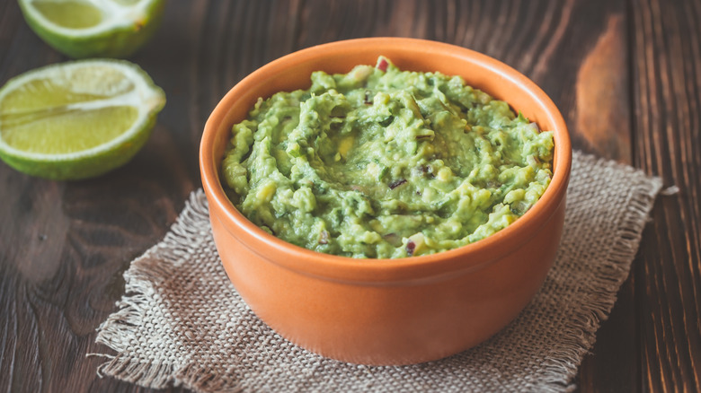 A bowl of guacamole surrounded by limes