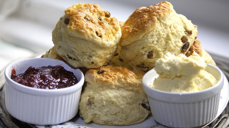 Scones with bowls of cream and jam are piled on a plate.