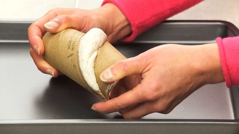 A pair of hands are shown opening canned biscuit dough.