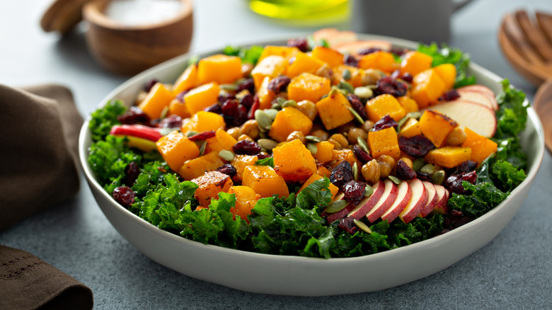 Kale salad with butternut squash, apples, dried cranberries in white bowl