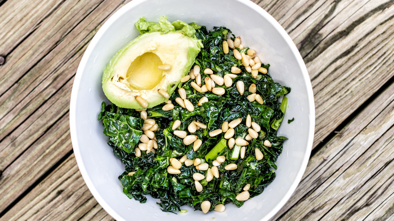 Massaged green kale salad with half avocado and pine nuts on wood table