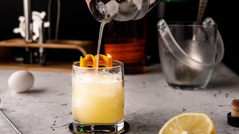 pouring a whiskey sour with lemon and egg