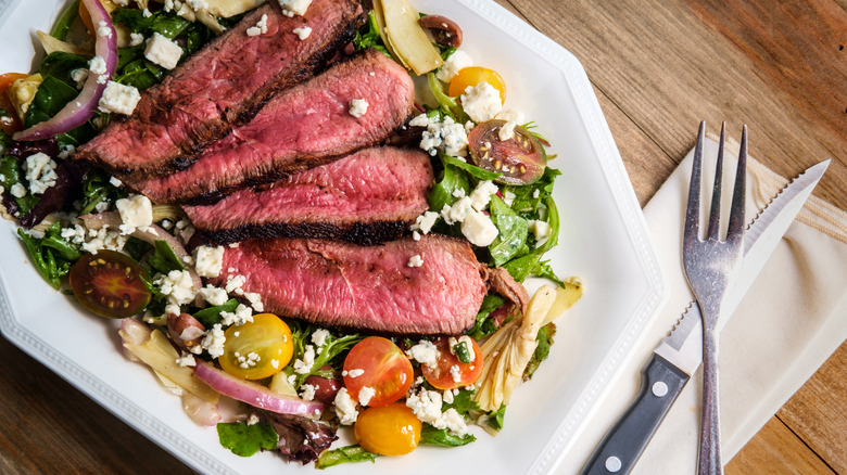 Slices of meat arranged atop a colorful salad on a large plate