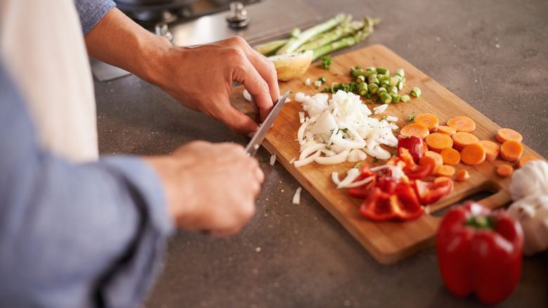 Closeup of a person's hands chopping vegetables on a wooden cutting board