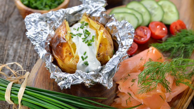 Baked potato filled with sour cream in foil with smoked salmon and salad ingredients