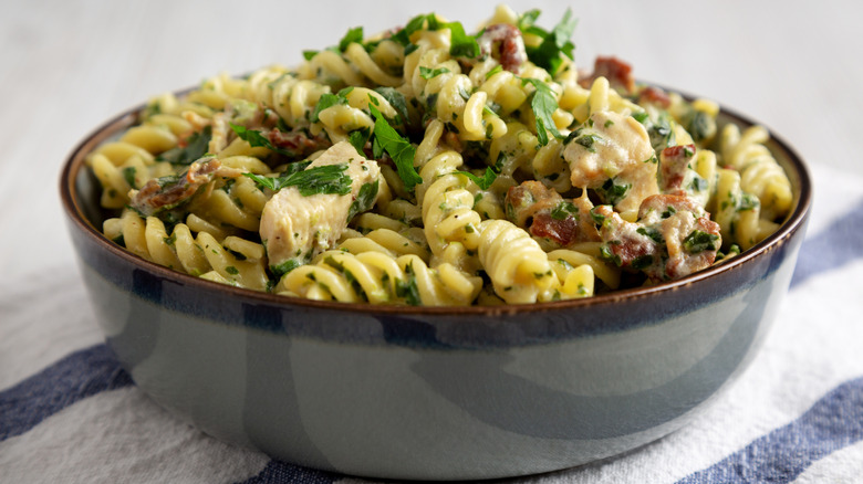 A bowl of rotini chicken Alfredo with fresh herbs sits on a tablecloth