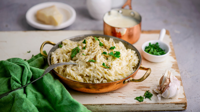 Alfredo pasta sits in a skillet, topped with fresh herbs