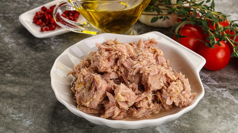 Canned tuna in a white dish with tomatoes, olive oil, and other items in the background