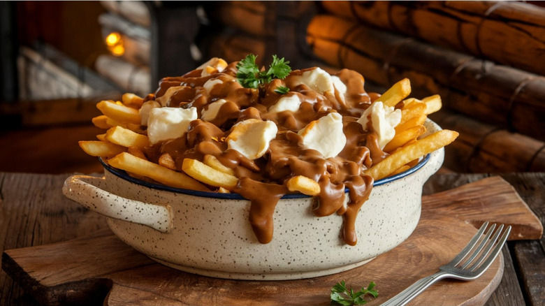 A bowl overflowing with poutine on a wooden cutting board