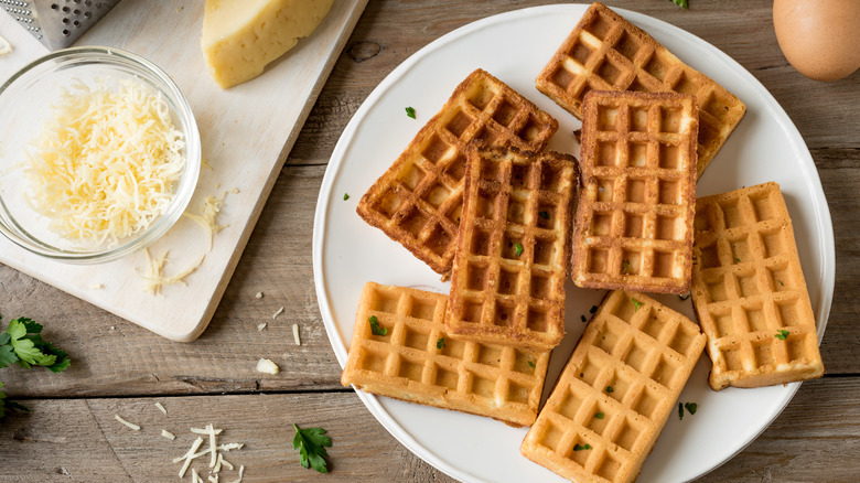 chaffles on a plate next to a bowl of shredded cheese and single brown egg