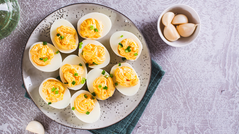 Plate of deviled eggs with bowl of garlic cloves next to it