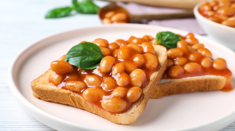 Baked beans on toast served on white plate with basil leaf