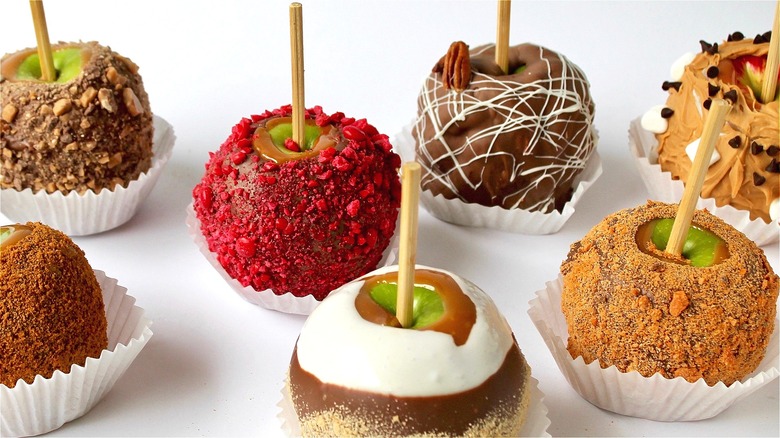 Caramel apples with a variety of toppings on white paper liners