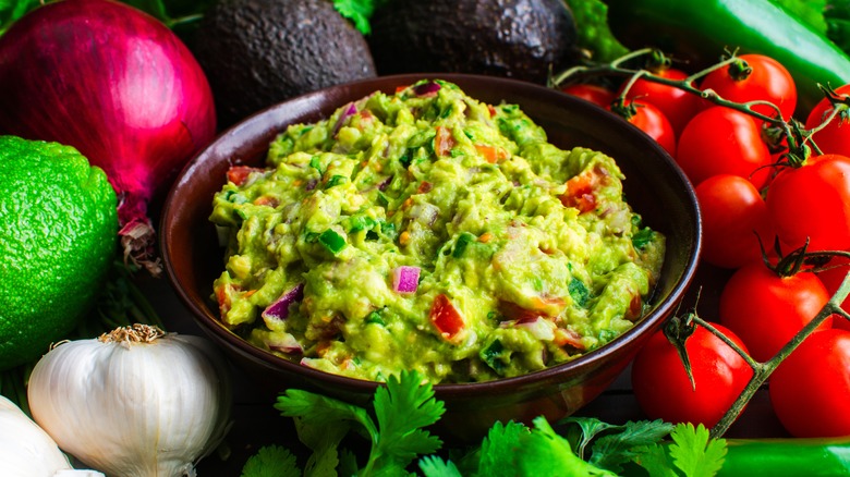 wooden bowl of guacamole surrounded by fresh veggies