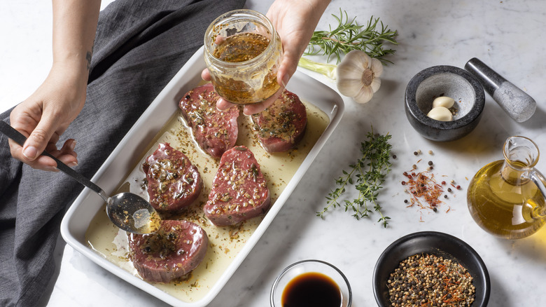 A hand spooning marinade over cuts of meat