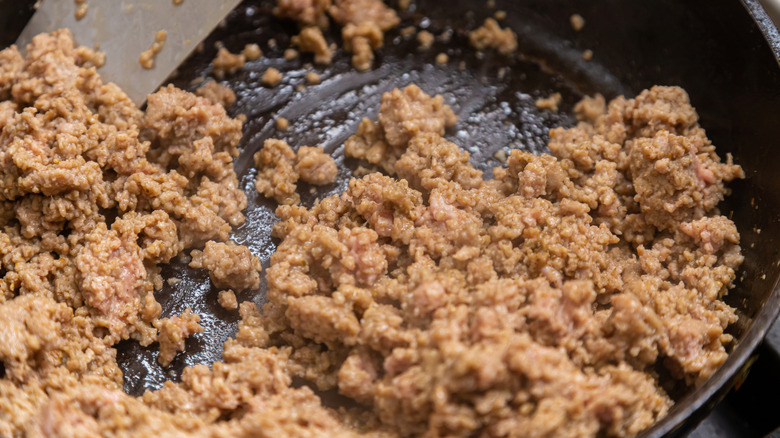 A closeup on ground beef being stirred in a skillet with a metal spatula.