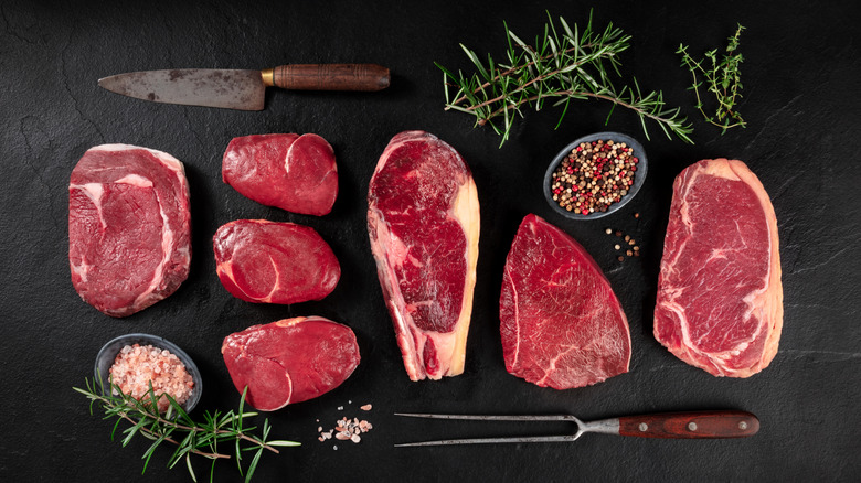 Various cuts of steak alongside seasonings and cooking implements