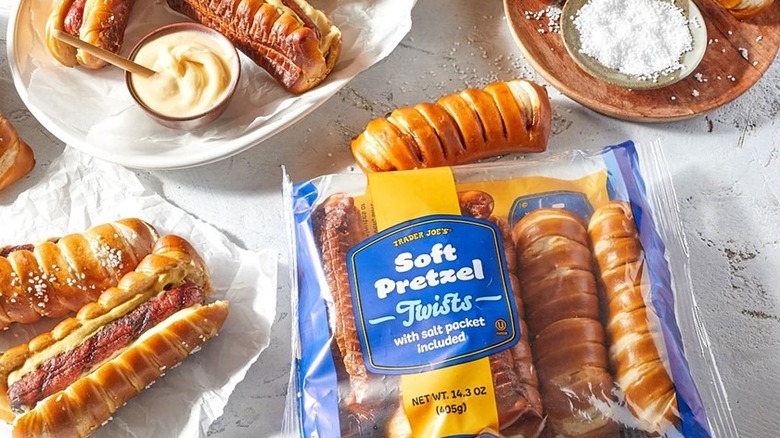 A package of Trader Joe's new Soft Pretzel Twists sits near pretzel dogs, a dish of white dipping sauce, and a dish of coarse salt